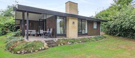 A modern house with a covered patio, a brick chimney, and a well-maintained garden.