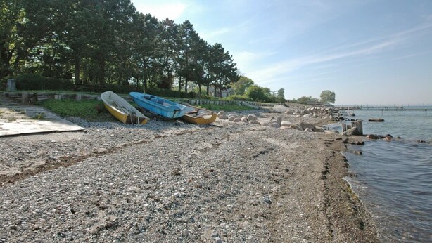 A pebbled beach with boats and a wooden pier extending into calm water.