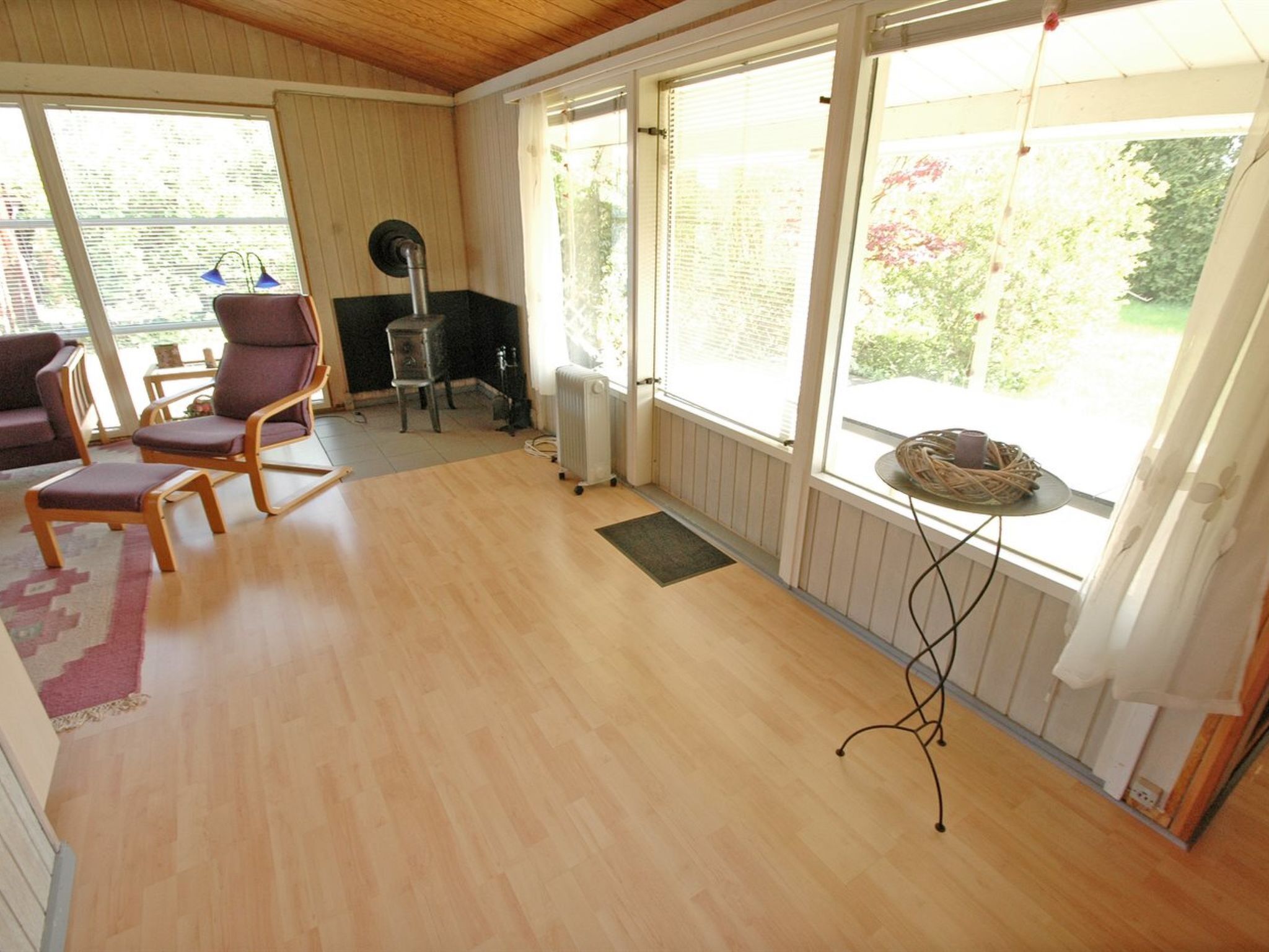 A room with wooden flooring, a radiator, a chair, a table, and a window with a view of greenery.