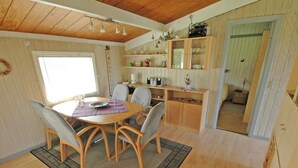 A cozy room with a wooden dining table, chairs, and a kitchen area with wooden cabinets and shelves.