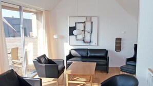 Ein modernes Wohnzimmer mit einer schwarzen Ledersofa, zwei schwarzen Ohrensesseln, einem Holztisch und einem großen abstrakten Gemälde an der Wand.