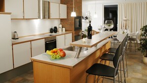 Eine moderne Küche mit weißen Schränken, einer Holz Arbeitsplatte und einer Obstschale. Es gibt einen Essbereich mit Tisch und Stühlen sowie eine Kühlpflanze.