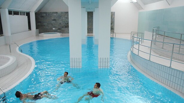 Ein Hallenbad mit klarem Wasser, einer Sprungplattform und einem gefliesten Boden.
