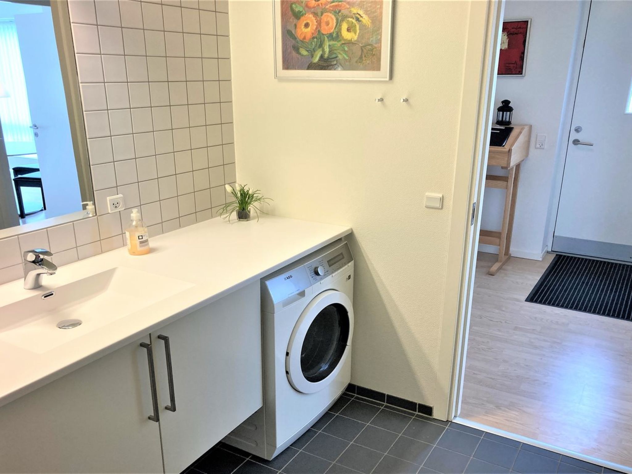 Ett litet och praktiskt tvättrum med tvättmaskin, handfat och en liten krukväxt.