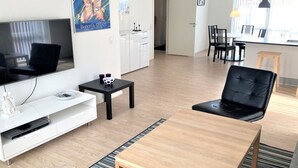 Een moderne woonkamer met een flatscreen televisie, een zwarte leren fauteuil, een houten salontafel en een klein zwart bijzettafeltje.