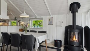 Un interior moderno con zona de comedor, estufa de leña negra y vistas a la vegetación.