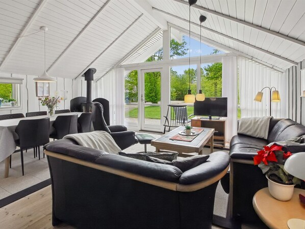 Una sala moderna con un sofá de cuero negro, un comedor con mesa y sillas, y un ventanal con vistas al exterior.