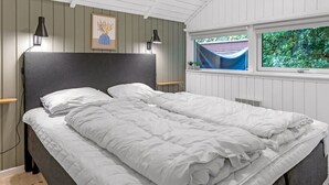 Un dormitorio con una cama grande, dos lámparas de noche, un ventanal con vistas a la vegetación y un cuadro en la pared.