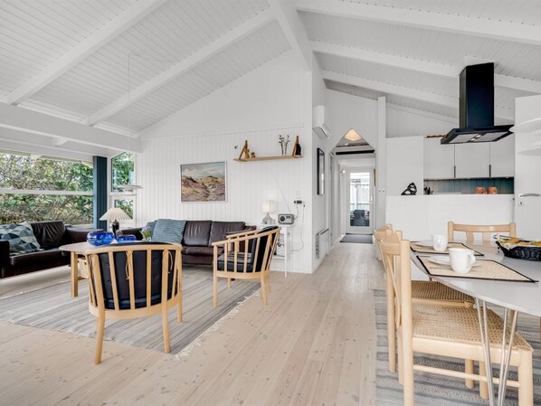 A spacious living area with a dining table, chairs, and a sofa. There is a kitchen area with cabinets and a stove.