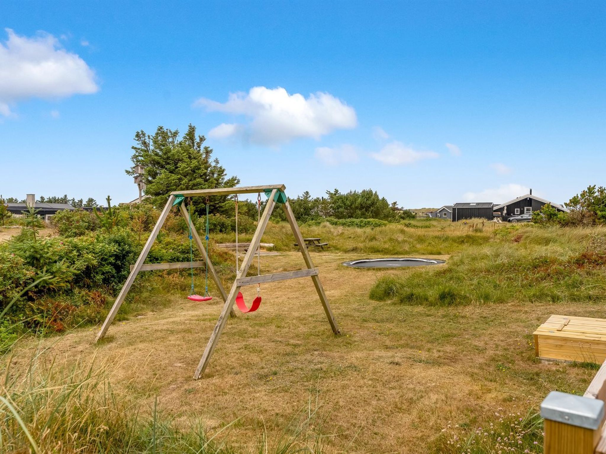 A playground with a swing set and a trampoline in a grassy area with houses in the background.