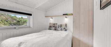 Een slaapkamer met een bed, een raam, een kast en een plank met boeken.