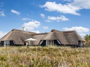 Et hus med stråtækt tag, en lille veranda og et vindue.