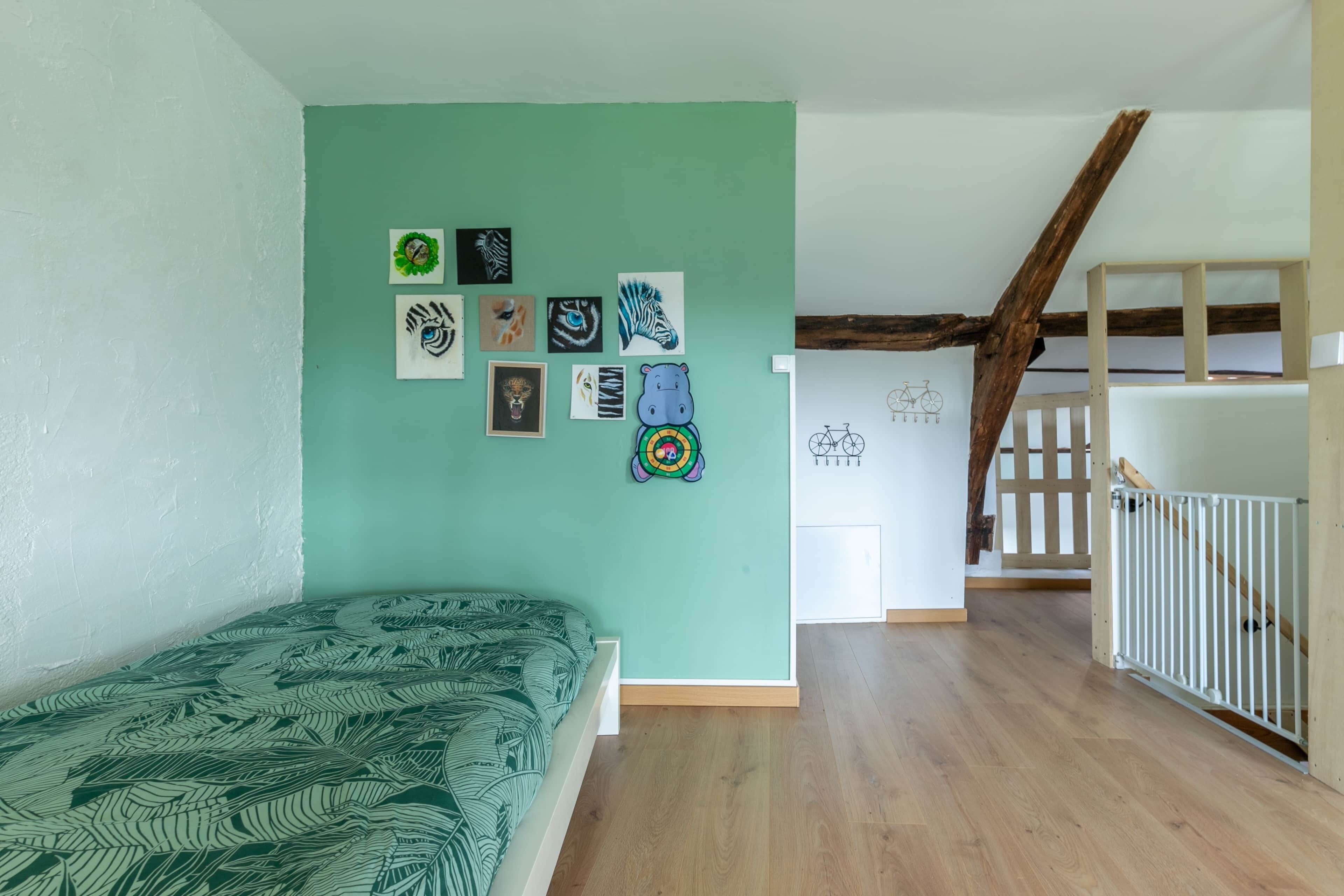Una stanza con un letto, una scala e un muro decorato con disegni per bambini.