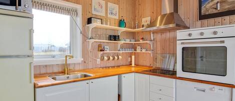 A compact kitchen with wooden paneling, a built-in oven, a microwave, and a sink with a wooden countertop.