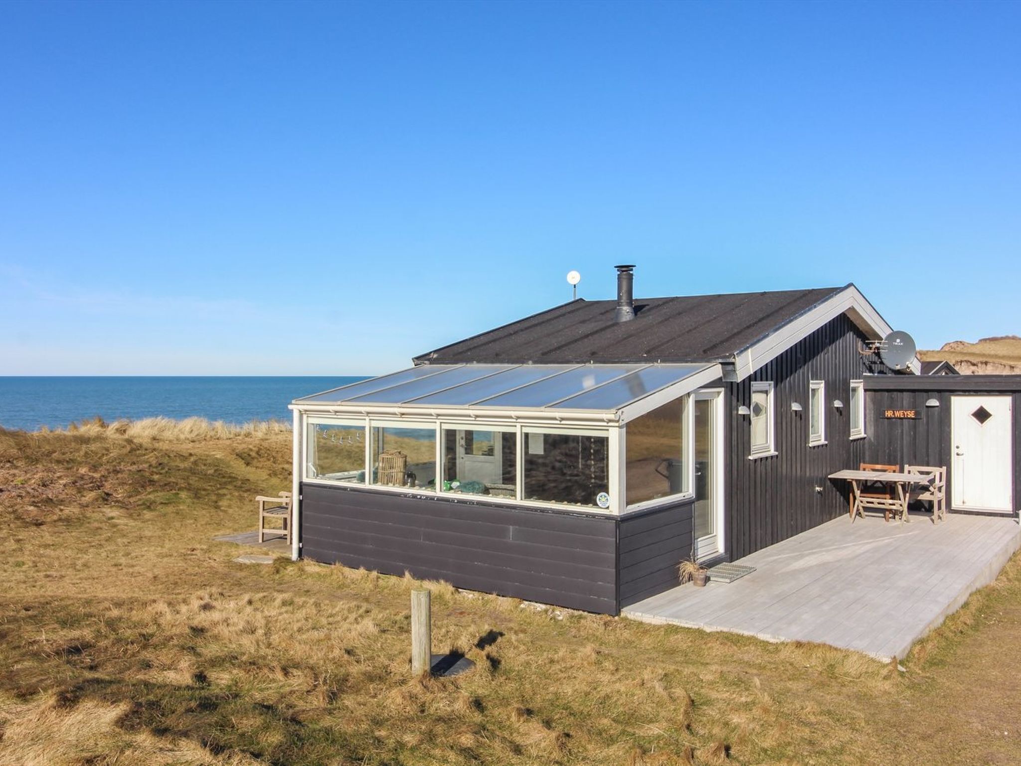 A modern coastal house with a glass-enclosed patio, a deck, and a view of the sea.