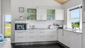 Een moderne keuken met witte kastjes, een inbouwoven, een koffiehoek en uitzicht op de omgeving.