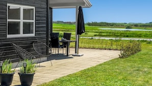 Een modern huis met een patio, met twee stoelen en een tafel, uitkijkend op een groen landschap.