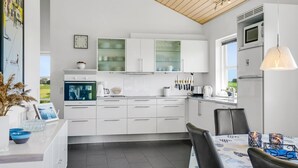 Een moderne keuken met witte kasten, een ingebouwde oven en een eethoek met een tafel en stoelen.