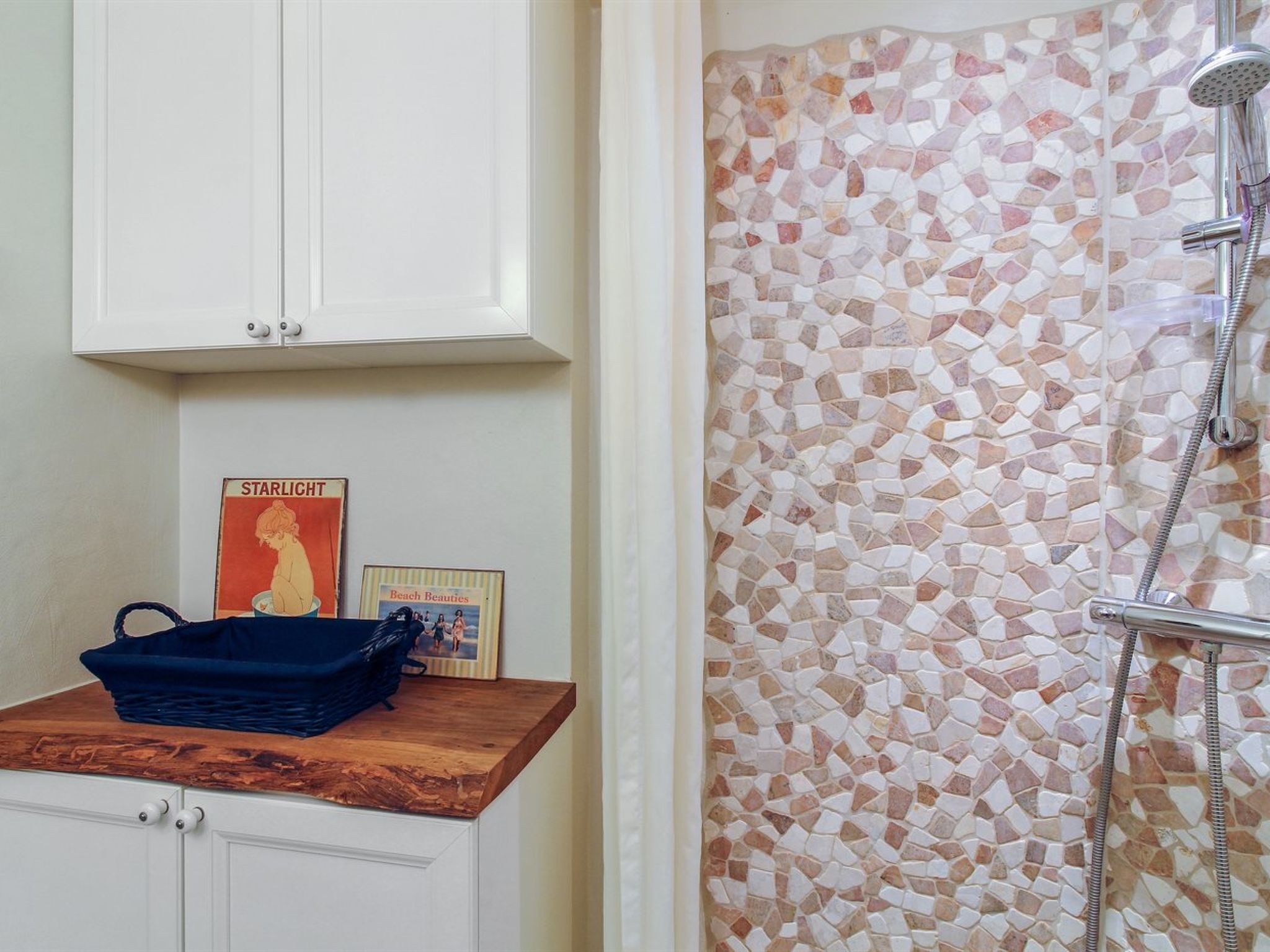 A bathroom with a shower area featuring mosaic tile, a wooden vanity, and a cabinet above.