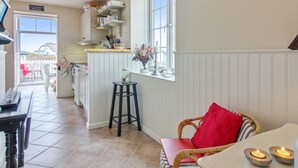Una cocina acogedora con comedor, que cuenta con un ventanal con vistas, un taburete pequeño y una silla de mimbre con un cojín rojo.