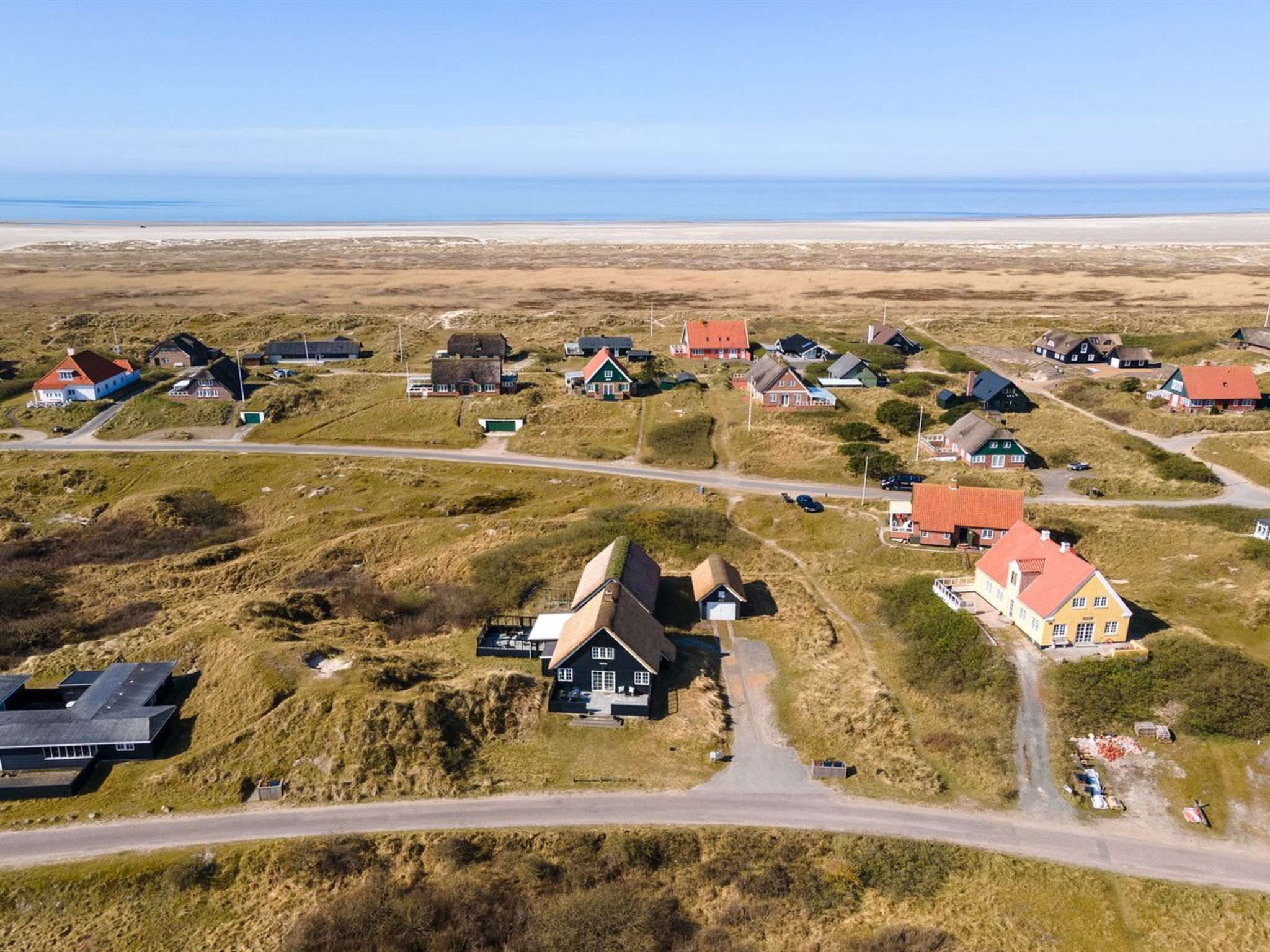 An aerial view of a coastal village with houses, roads, and a beach.