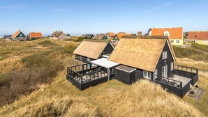A coastal house with a thatched roof, a deck, and a view of other houses in the background.