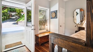 A bedroom with a wooden ceiling, a door leading outside, a bedside table, a bed, a mirror, and a wall with a circular artwork. - 16 mi to DT, Hot Tub, Fire Pit, FP, Basket Ball Court, Mt View, Secluded & Quiet (Barnardsville)