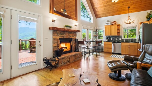 A spacious living area with a stone fireplace, wooden ceiling, and a view of a deck. - 16 mi to DT, Hot Tub, Fire Pit, FP, Basket Ball Court, Mt View, Secluded & Quiet (Barnardsville)