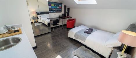 A modern bedroom with a skylight, a bed, a desk, and a mirror.