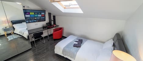 A modern bedroom with a skylight, a bed, a desk, and a red chair.