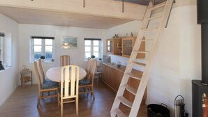 Ein geräumiger Essbereich mit rundem Tisch und Stühlen, eine Küche mit Holzschränken sowie eine erhöhte Schlafkoje mit einer Leiter.