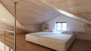 Ein Schlafzimmer mit schrägem Dach, einem Bett, einem Fenster und einem Metallgeländer.