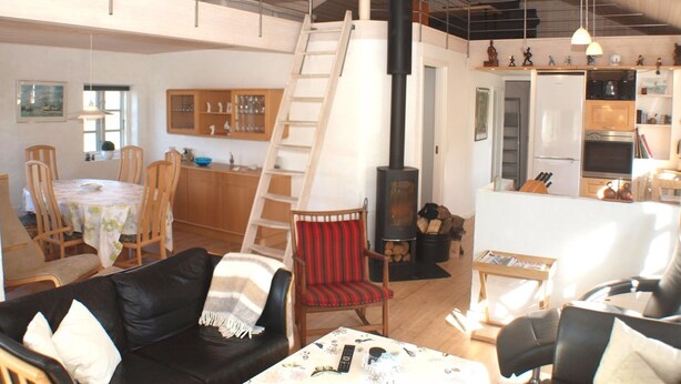 Ein großzügiger Wohnbereich mit hoher Decke, einem zentralen Kamin, Holzmöbeln und einer Küchenzeile mit modernen Geräten.