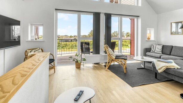 Een ruime woonkamer met een groot raam, een bank, een televisie en een balkon met uitzicht op het landschap.