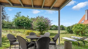 Un patio exterior con una zona de estar techada, una mesa y sillas.