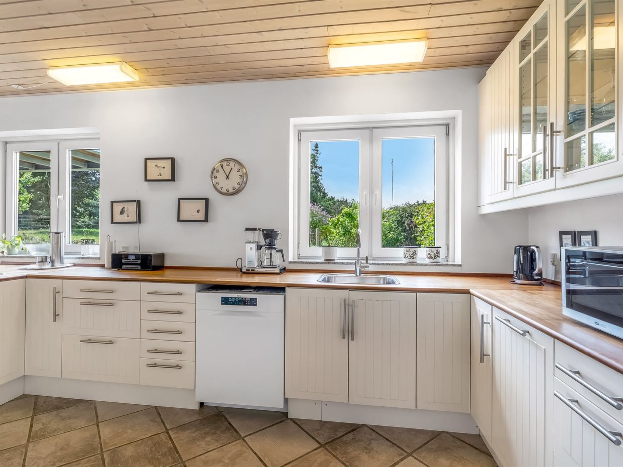 Une cuisine moderne avec des meubles blancs, un lave-vaisselle encastré, une machine à café et une grande fenêtre offrant une vue sur la verdure.
