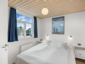 A bedroom with a large bed, a window with curtains, a poster on the wall, and bedside tables.