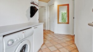Un espace buanderie comprenant un lave-linge, un étendoir et une porte donnant sur une pièce avec une fenêtre.