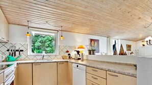Une cuisine moderne avec des meubles en bois, un four encastré, un lave-vaisselle et une fenêtre donnant sur la verdure environnante.