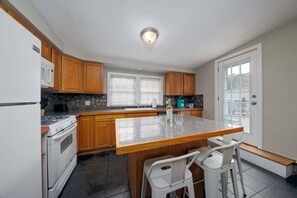 Una cocina con armarios de madera, encimera de granito, estufa y un comedor con dos sillas.