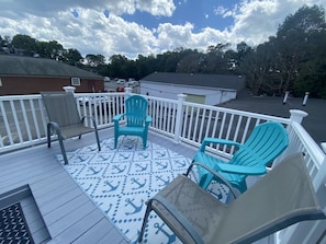 A deck with chairs, a patterned rug, and a white railing.