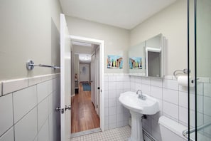A bathroom with a white sink, a glass shower enclosure, and a door leading to a hallway with a wooden floor.