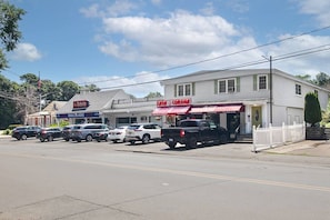 A street view with a row of parked cars, a building with a red awning, and a white picket fence.