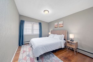 Un dormitorio con cama, lámparas de noche, una ventana con cortinas y una obra de arte colgada en la pared.