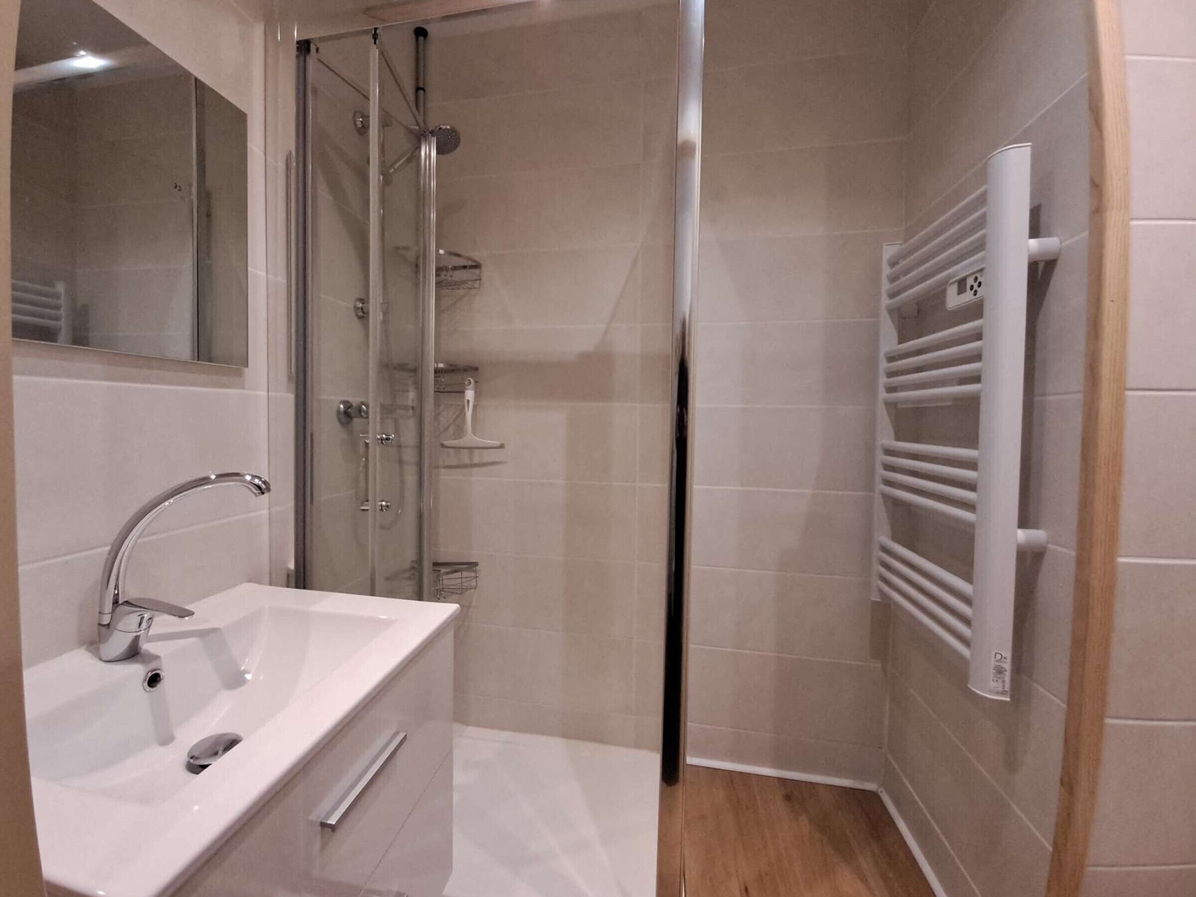 A modern bathroom with a glass shower enclosure, a white sink with a chrome faucet, and a built-in towel rack.