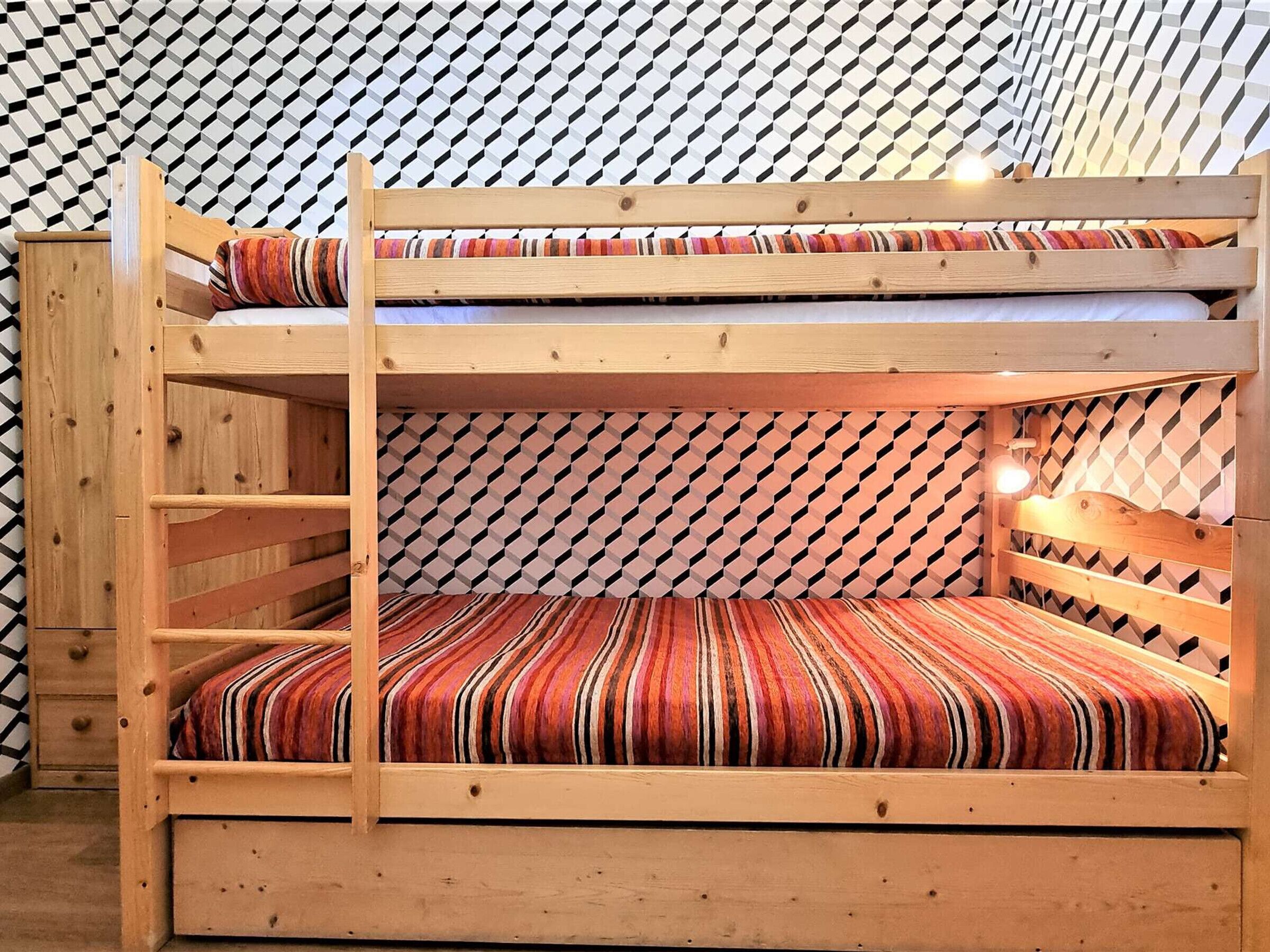 A bunk bed with a striped mattress and a geometric patterned wall behind it.