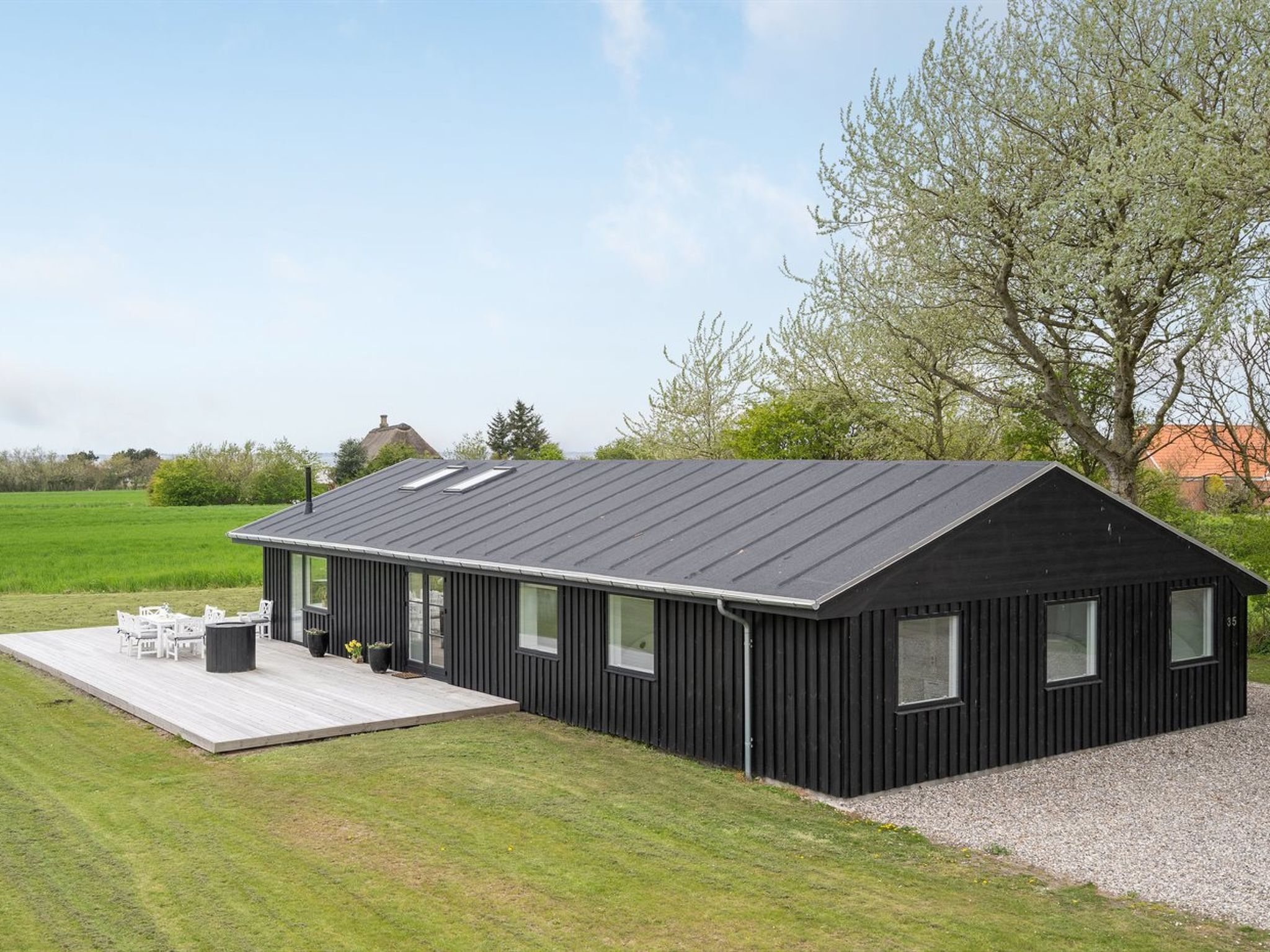 Un bâtiment moderne de couleur noire, doté d’un toit en pente, de grandes fenêtres et d’une terrasse en bois aménagée avec du mobilier d’extérieur.