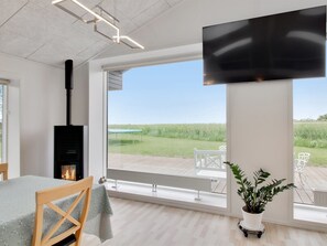A modern room with a fireplace, a large TV, and a view of a grassy field. - Vacation home "Ajla" by Interhome (Bredebro)