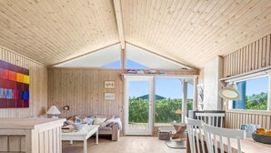 Un interior de madera con zona de comedor, un sofá y vistas a través de un ventanal.
