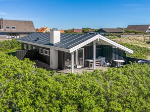 A modern house with a sloped roof, a deck with outdoor furniture, and a view of surrounding houses.